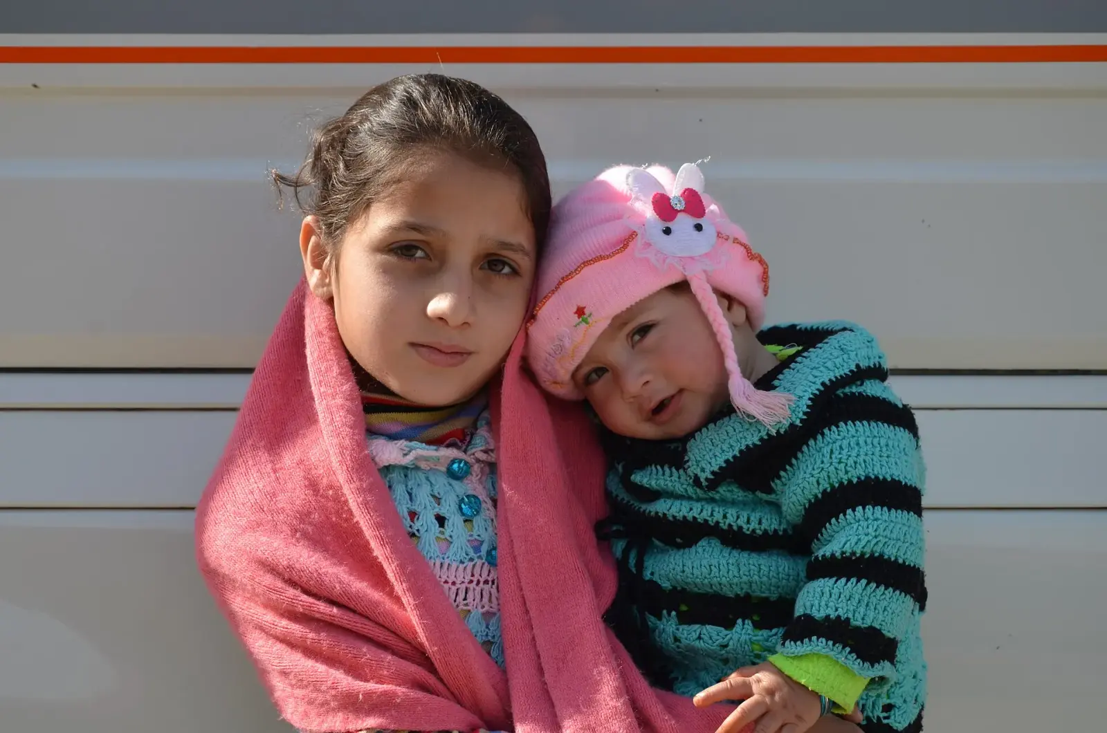 A girl wrapped in a pink shawl holding a baby in a knitted cap