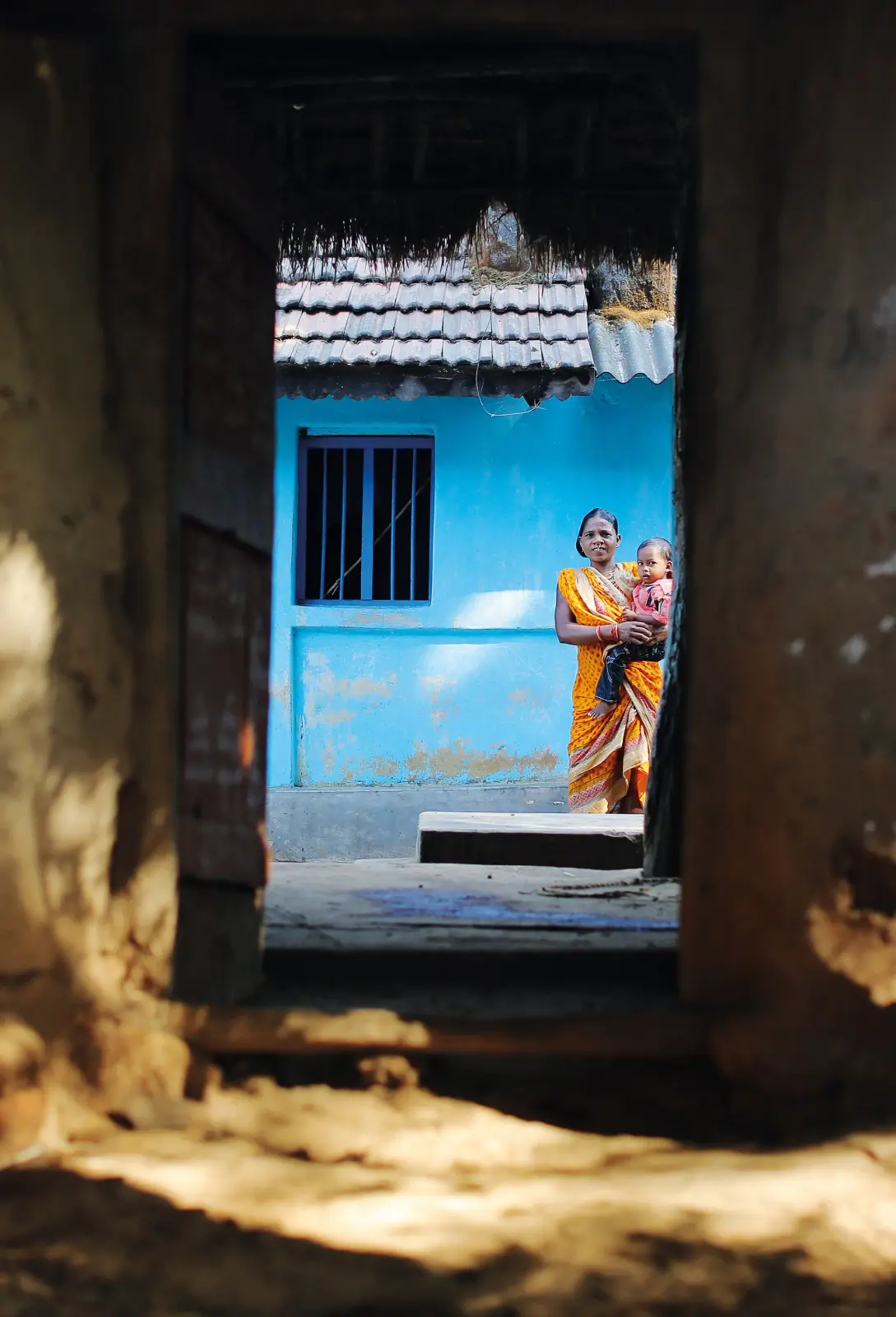 A mother holding her child at the doorway of a blue home
