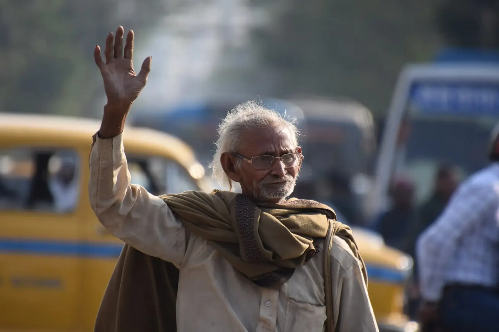 An elderly man waving on a busy city street